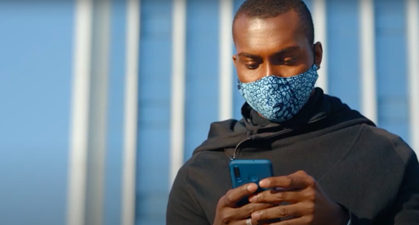 Man wearing mask looking at smartphone to take symptom screening assessment